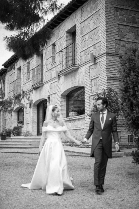The bride and groom walk hand in hand outside the historic stone buildings of Cigarral de la Mercedes.