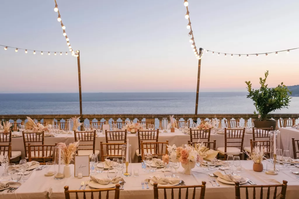 Elegant outdoor wedding reception at Domaine de Canaille with string lights, blush florals, and panoramic sea views at sunset.
