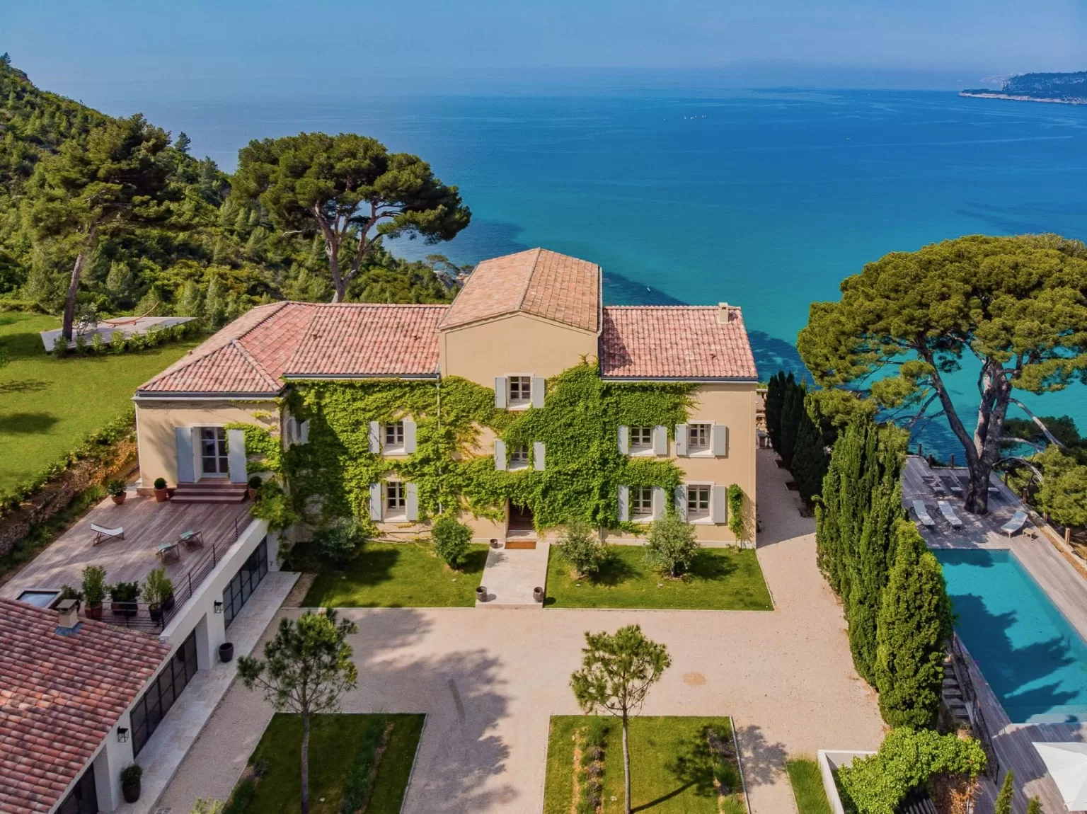 Aerial view of Domaine de Canaille villa with terracotta roof and lush greenery overlooking the turquoise Mediterranean Sea.