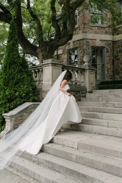 Bride with a flowing veil walking up the stone staircase of Graydon Hall.