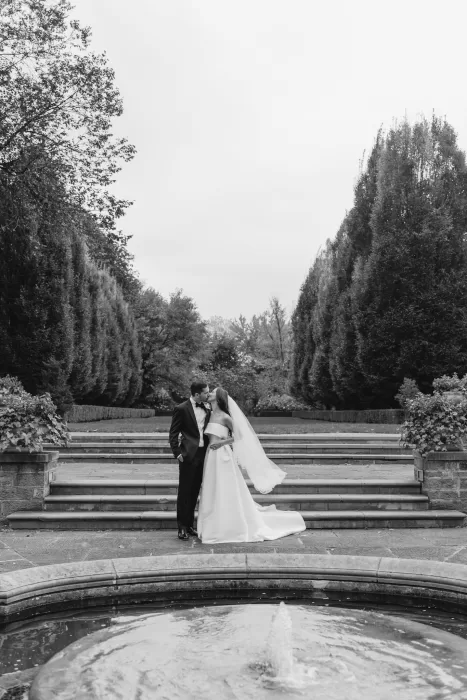 Bride and groom sharing a kiss by the fountain in the formal gardens of Graydon Hall.
