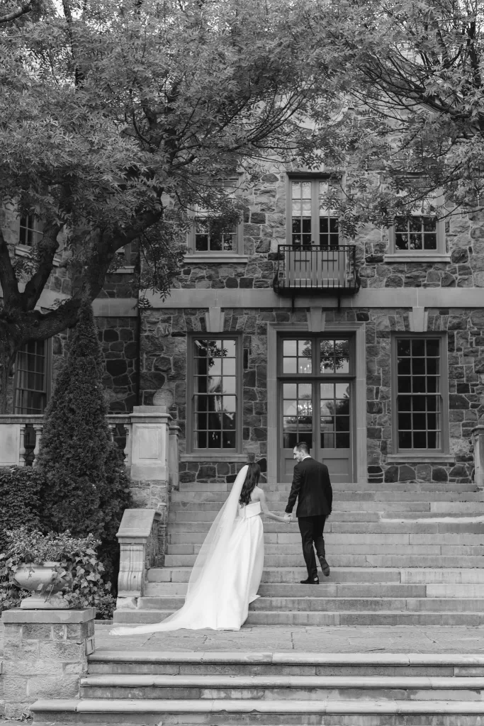 Black and white photo of the bride and groom walking hand in hand up the stone steps of Graydon Hall.