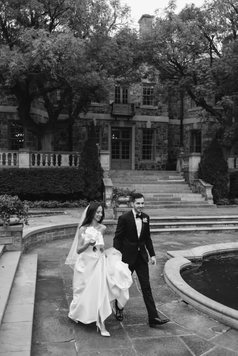 Bride and groom walking together beside the fountain in the stone courtyard of Graydon Hall.