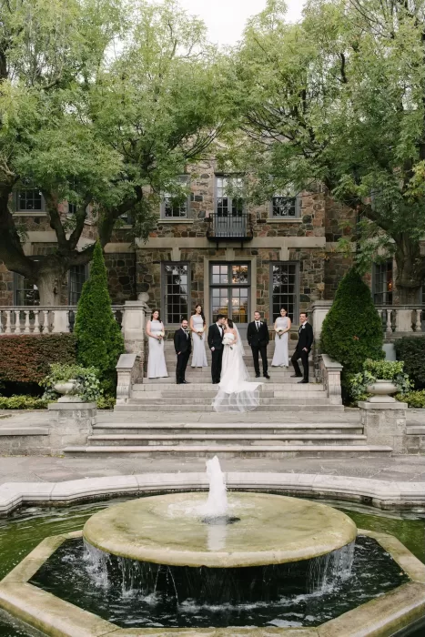 Bride and groom with their wedding party gathered by the fountain and stone steps of Graydon Hall.