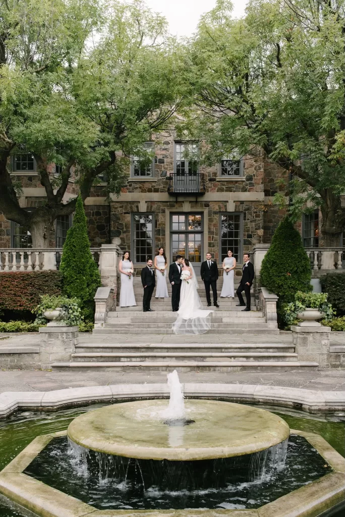 Bride and groom with their wedding party gathered by the fountain and stone steps of Graydon Hall.