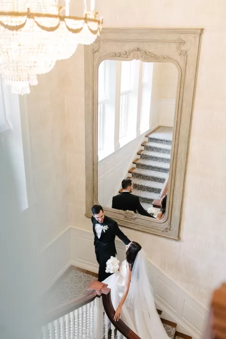 Bride and groom captured in the grand mirror while walking the elegant staircase inside Graydon Hall.