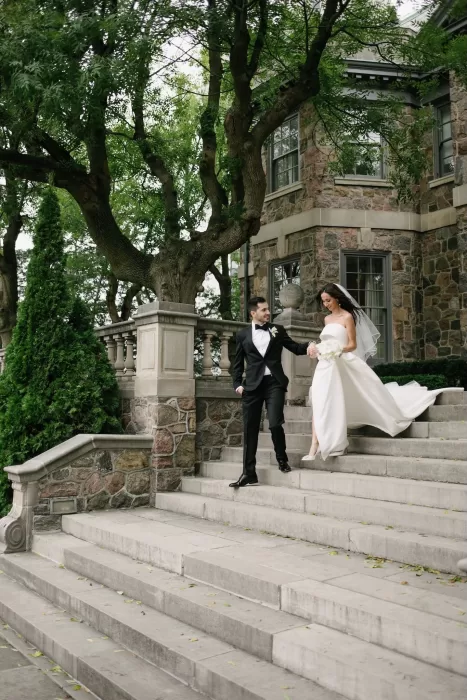 Bride and groom walking down the grand stone steps of Graydon Hall surrounded by lush greenery.