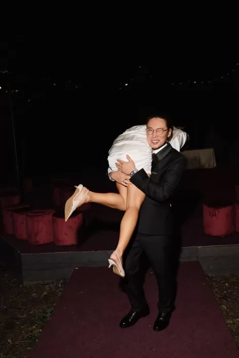 Groom carrying bride playfully over his shoulder during evening wedding celebration.