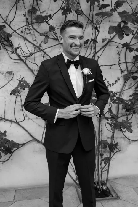 Groom smiling in a tuxedo against ivy-covered walls at Middleton Lodge.