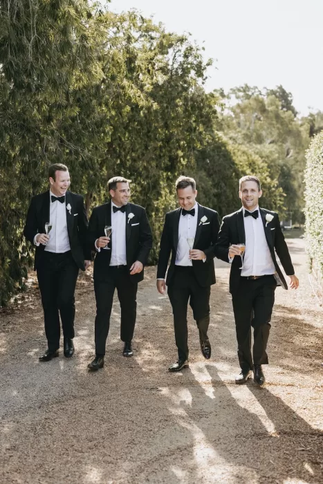 Groom and groomsmen walking down a tree-lined path with champagne in hand at Le Mas Barossa.