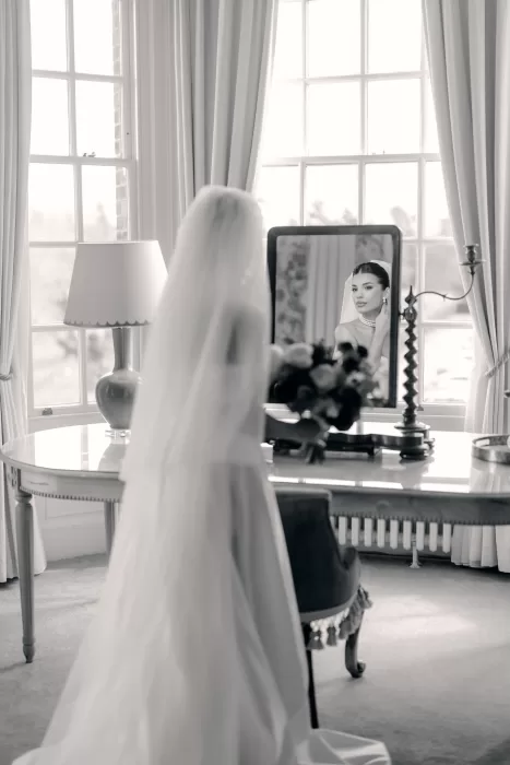 Bride gazing into mirror with bouquet in hand, veil flowing behind at Hedsor House.