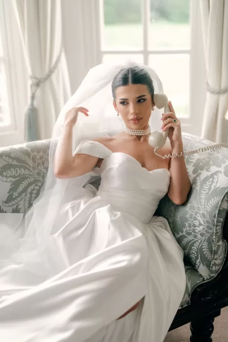 Bride reclining on sofa in her wedding gown, holding vintage telephone at Hedsor House.