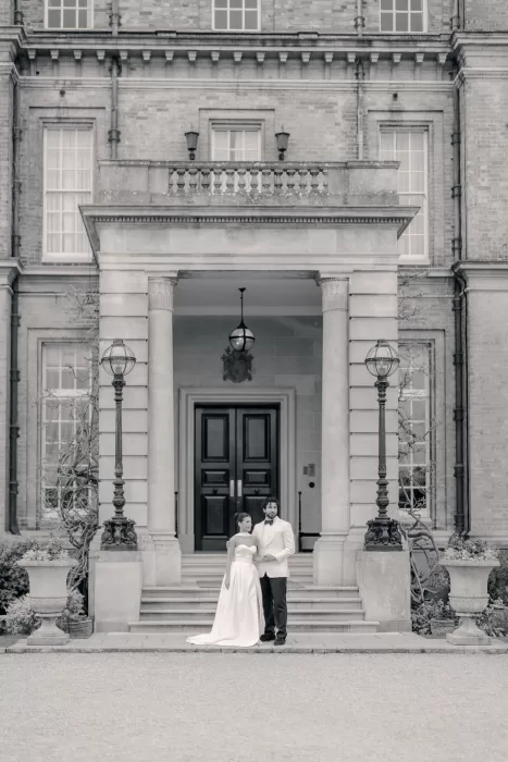 Black and white photo of couple standing at the grand entrance of Hedsor House.