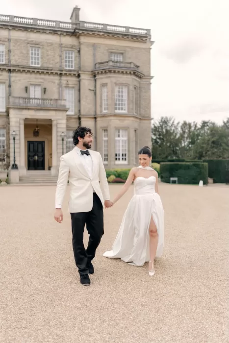 Bride and groom holding hands while walking across the grand courtyard at Hedsor House.