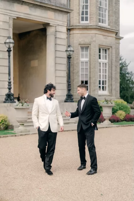 Two groomsmen in tuxedos talking outside the grand entrance of Hedsor House.