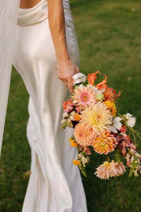 Close-up of the bride holding a vibrant bouquet of dahlias and summer blooms at La Farinera de Sant Lluis.