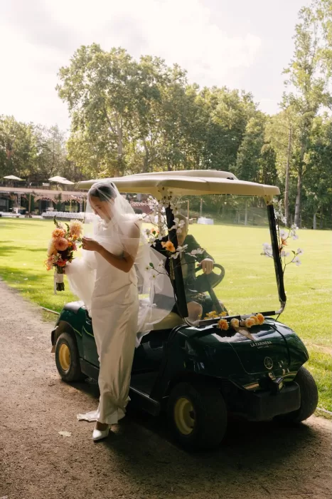 Bride stepping from a decorated golf cart with her bouquet at La Farinera de Sant Lluis.