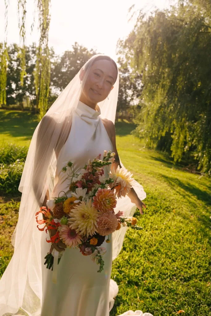Bride standing in golden sunlight holding a colorful bouquet at La Farinera de Sant Lluis.