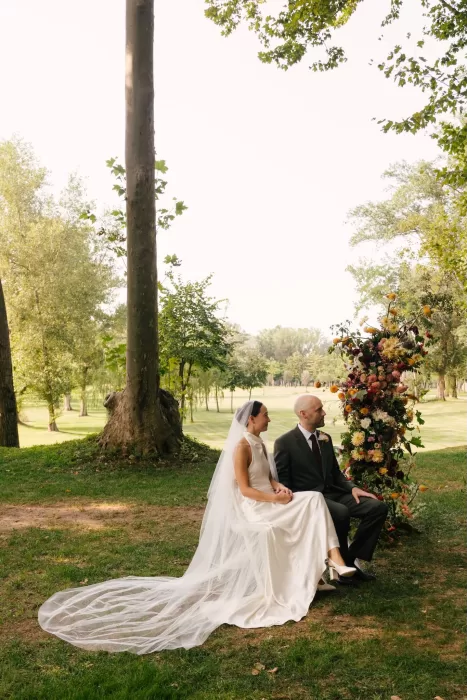 Bride and groom seated beside a floral arch during their outdoor ceremony at La Farinera de Sant Lluis.