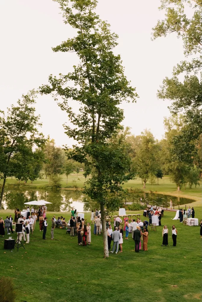 Wedding guests mingling on the lawn by the lake during cocktail hour at La Farinera de Sant Lluis.