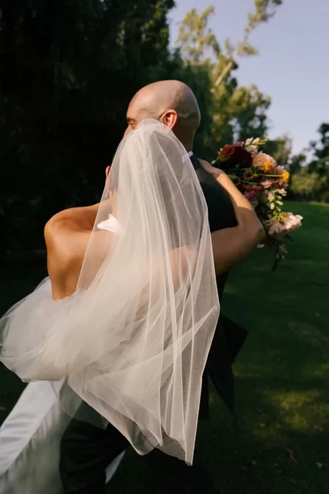 Groom holding bride with her veil flowing in the sunlight at La Farinera de Sant Lluis.