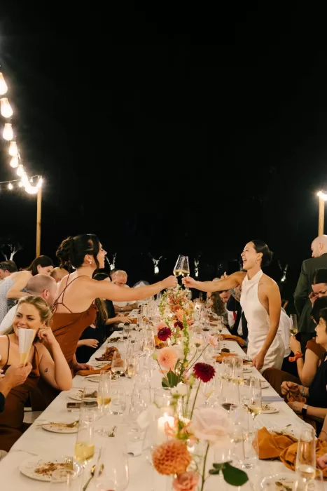 Bride raising a glass across the long candlelit dinner table during the reception at La Farinera de Sant Lluis.