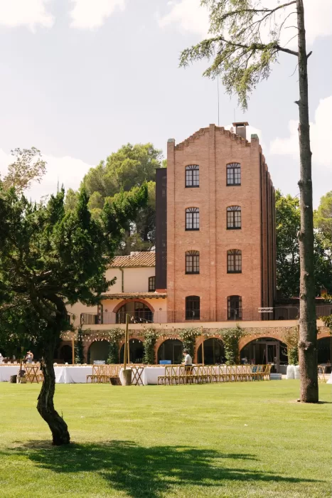 View of the historic brick building and lawns set for a wedding at La Farinera de Sant Lluis.