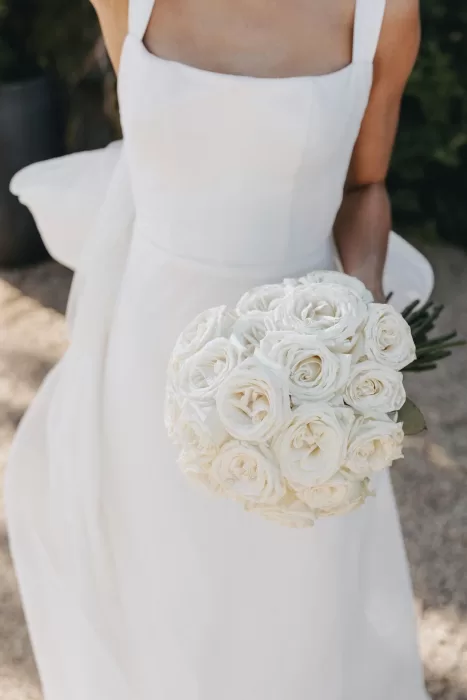 Bride holding a round bouquet of white roses, the structured bodice of her gown visible in soft sunlight at Le Mas Barossa.