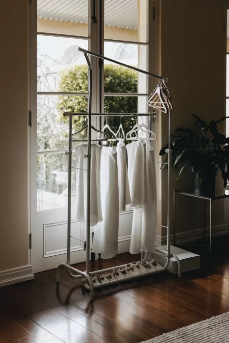 Bridesmaid dresses and shoes neatly hung on a rack by the window at Le Mas Barossa, with soft morning light filling the room.