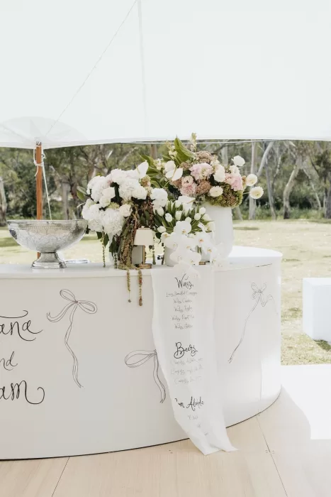 Curved white bar decorated with romantic floral arrangements and handwritten drinks menu at Le Mas Barossa.