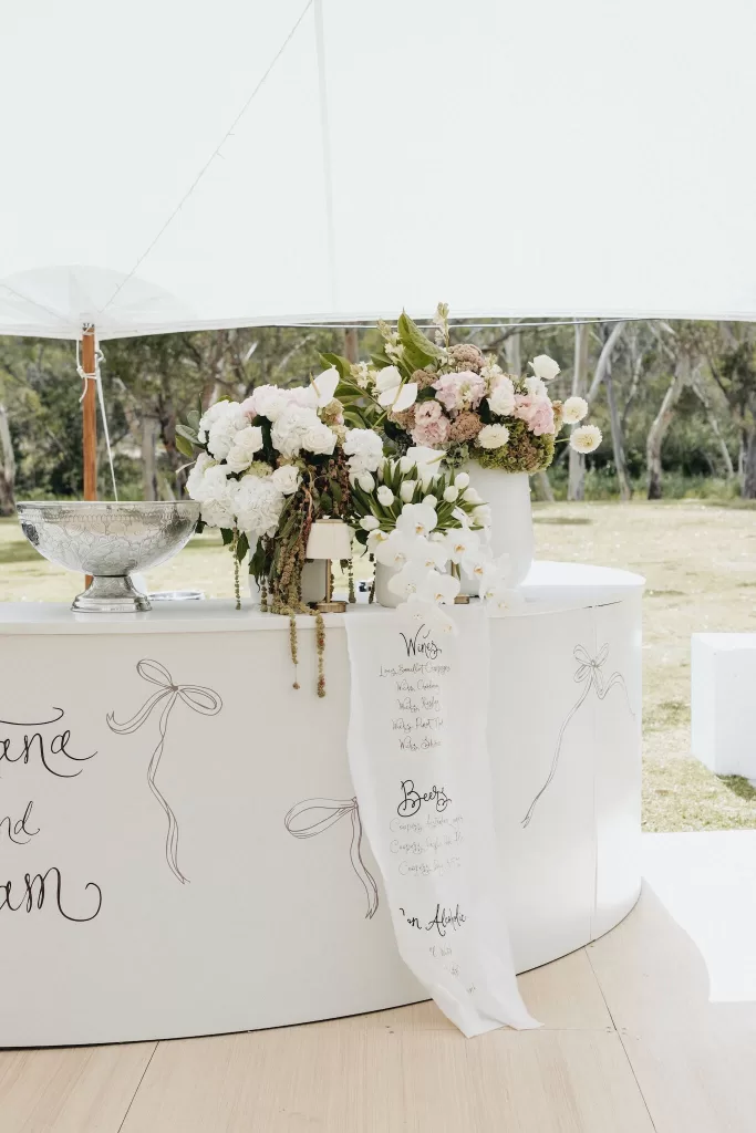 Curved white bar decorated with romantic floral arrangements and handwritten drinks menu at Le Mas Barossa.