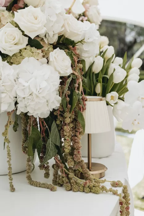 Elegant white roses, hydrangeas, and tulips cascading over the edge of a table at Le Mas Barossa, styled with a soft gold lamp.