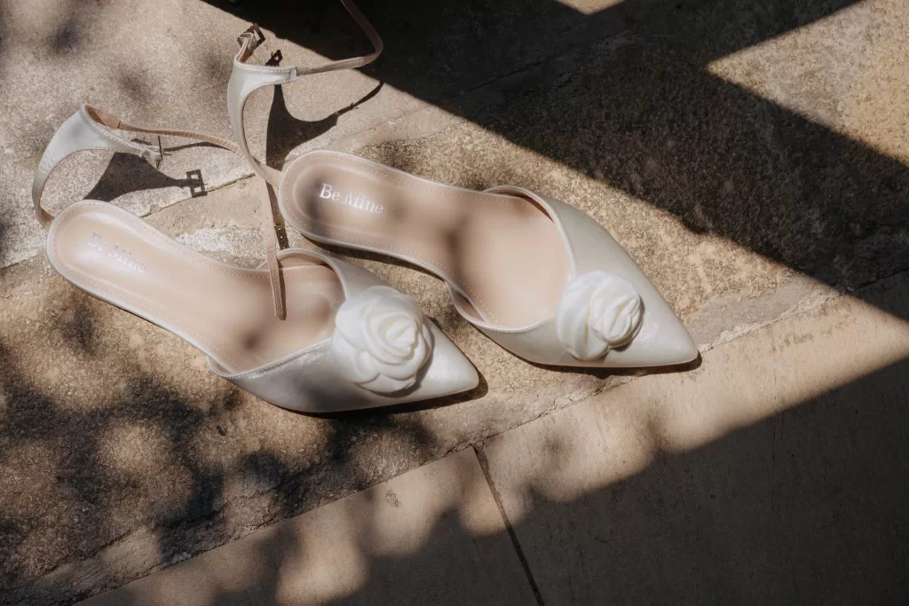 Elegant bridal shoes with white floral details photographed in sunlight at Liopetro.