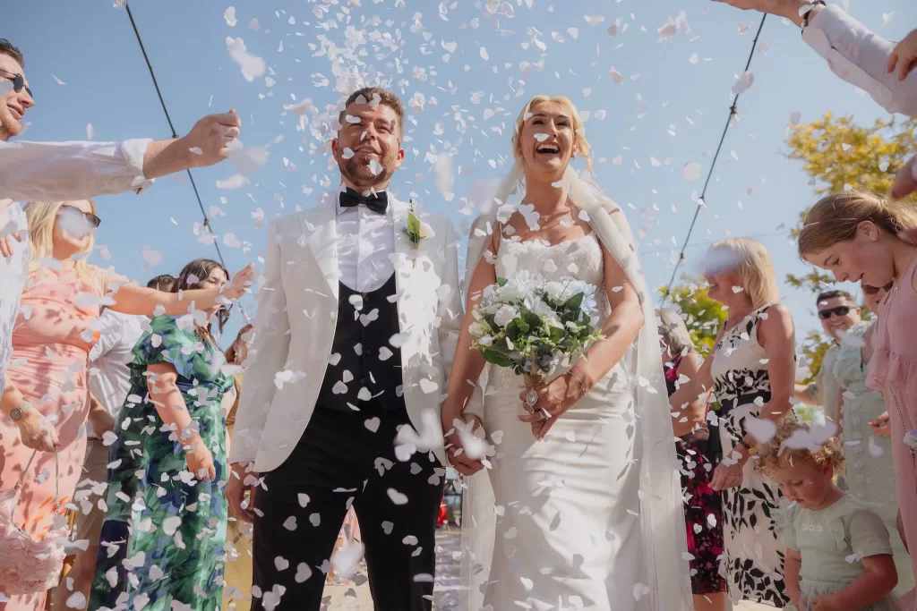 Bride and groom walking through a shower of confetti at Liopetro, surrounded by cheering guests.