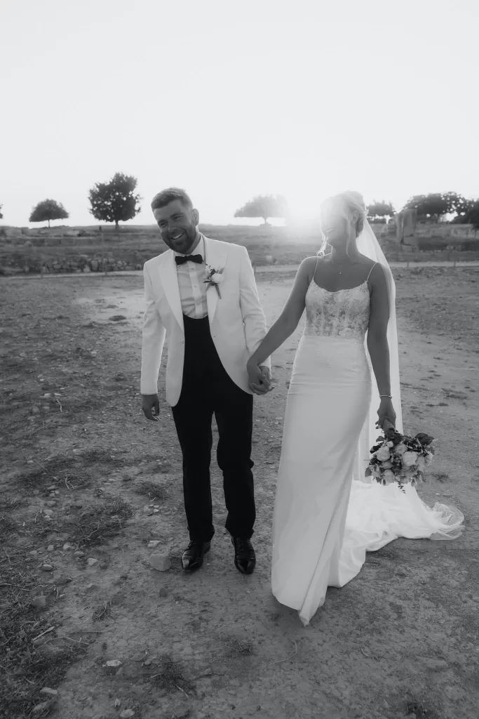 Bride and groom walking hand in hand at Liopetro during golden hour, smiling together.