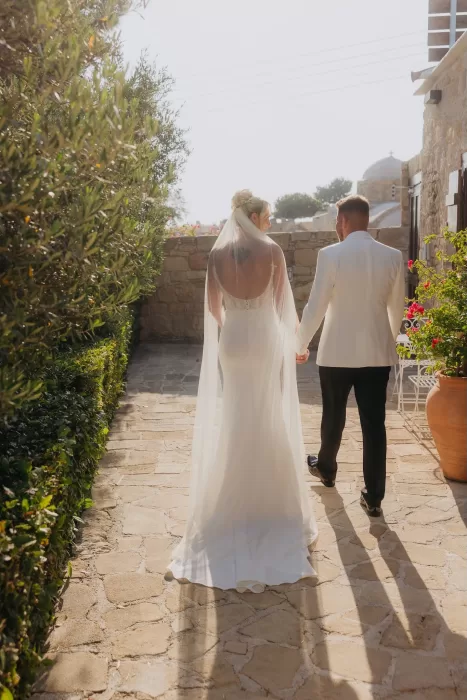 Bride and groom walking through the stone courtyard at Liopetro, captured from behind.