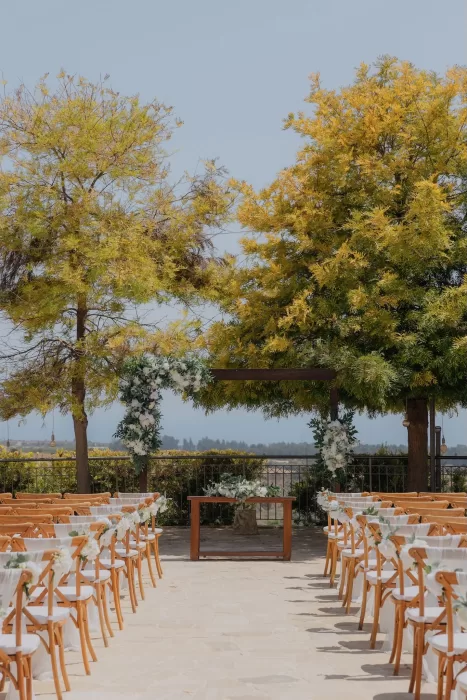 Outdoor wedding ceremony setup at Liopetro with wooden chairs, floral arch, and trees framing the aisle.