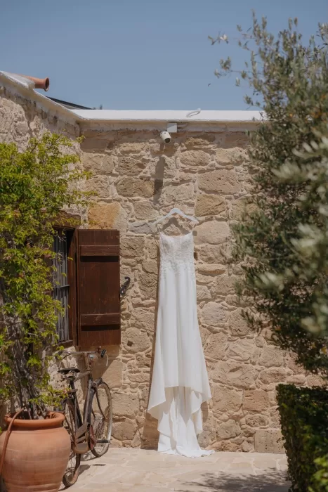 Elegant wedding dress hanging against a rustic stone wall at Liopetro before the ceremony.