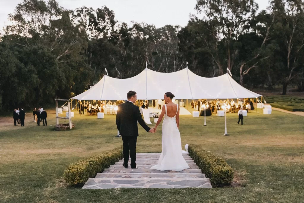 Bride and groom walking toward a glowing marquee reception tent at twilight at Le Mas Barossa.