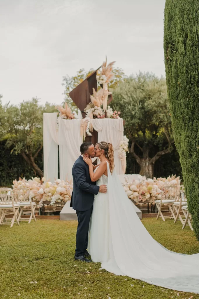 Bride and groom sharing a kiss in front of the floral ceremony altar at Mas de Les Voltes.