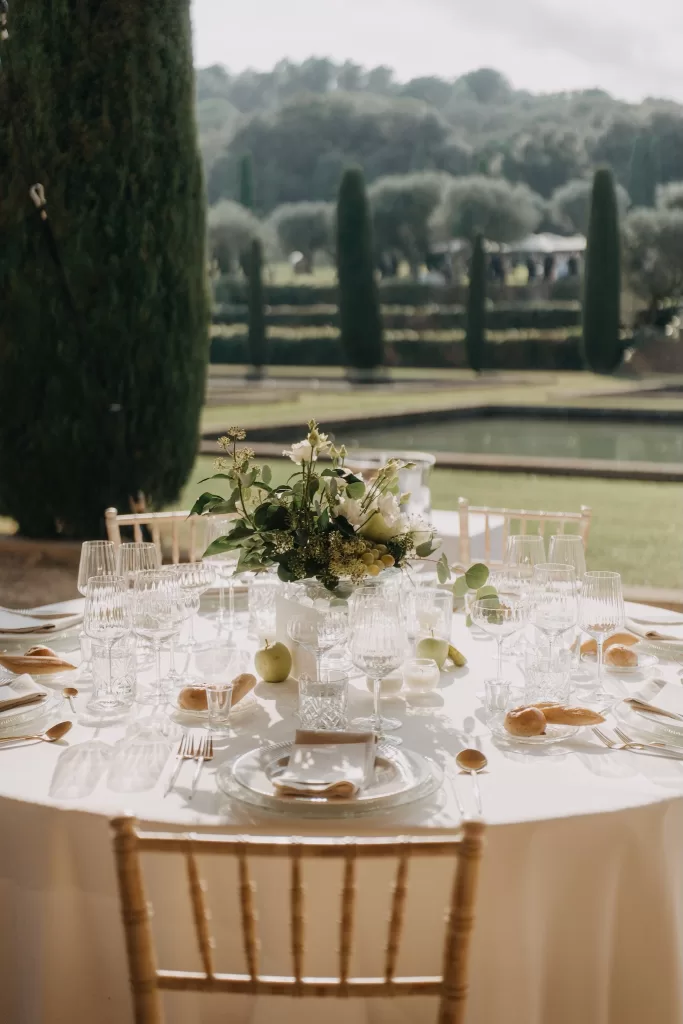 Elegant outdoor reception table set beside the reflecting pools at Mas de Les Voltes, styled with glassware and floral details.