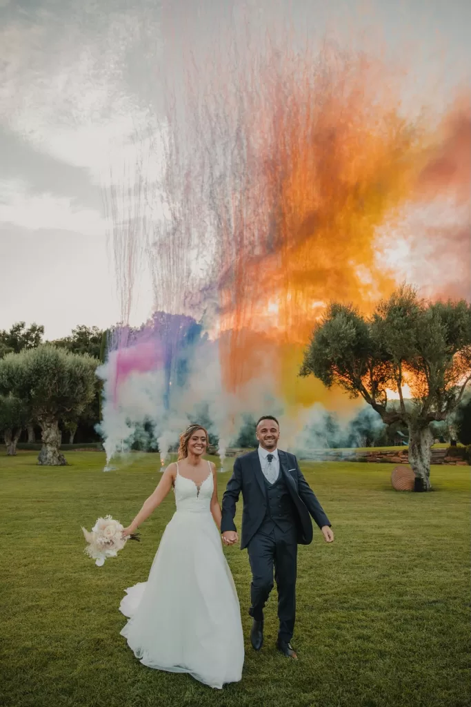 Bride and groom walking hand in hand with colorful smoke display at Mas de Les Voltes.