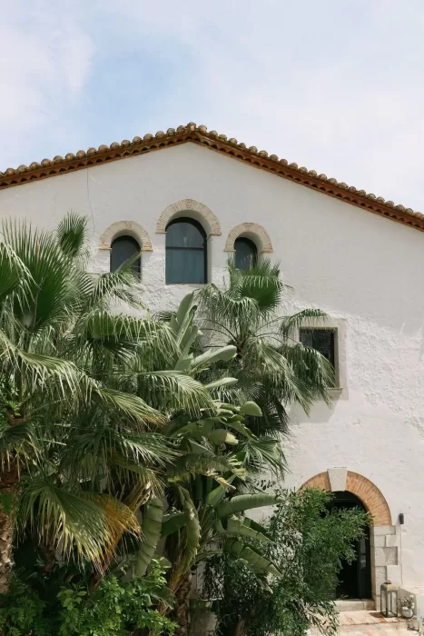 Whitewashed stone facade of Masia Victoria framed by lush palm trees.