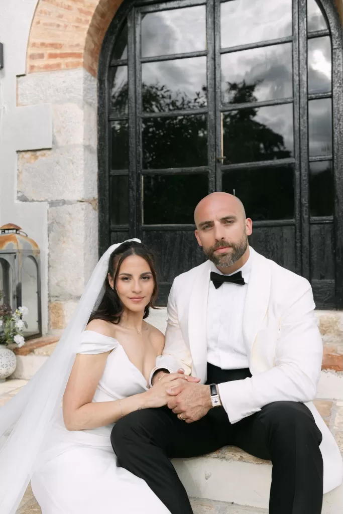 Bride and groom holding hands while seated on the stone steps outside Masia Victoria.