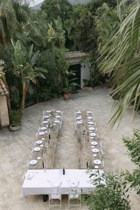 Elegant long-table wedding dinner setup in the courtyard of Masia Victoria surrounded by tropical greenery.