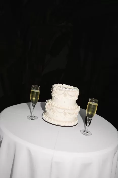 Two-tier white wedding cake with champagne flutes on a round table at Masia Victoria.
