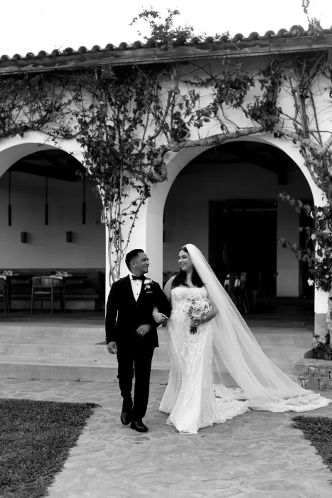 Bride and groom walking arm in arm under vine-covered arches at Minos Beach Art Hotel.