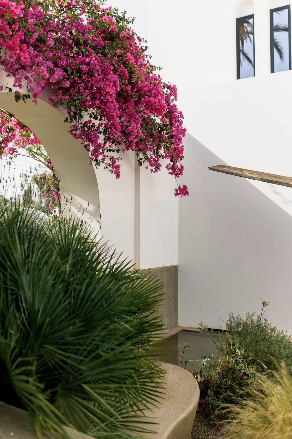 Pink bougainvillea cascading over white arch with lush greenery at Minos Beach Art Hotel.