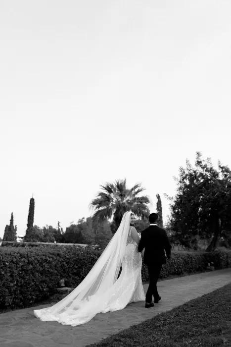 Black and white image of bride looking over her shoulder while walking hand in hand with groom at Minos Beach Art Hotel.