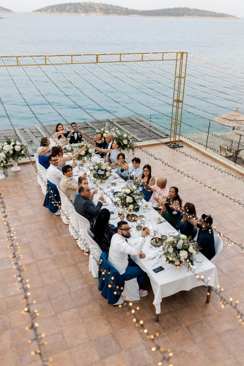 Black-and-white image of guests raising glasses during seaside wedding dinner at Minos Beach Art Hotel.